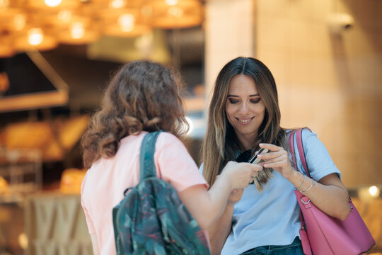 Smiling Young Woman Showing Her Smartphone Screen To A Friend Outdoors. Two happy female friends looking at mobile phone content together on city street 