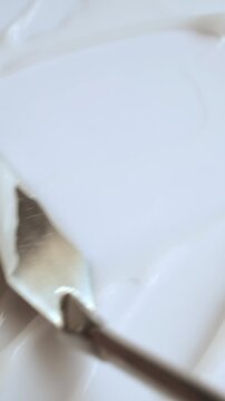 Thick white cosmetic cream being smoothed with a metal spatula creating a textured background