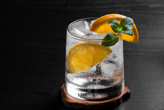 Refreshing Citrus Cocktail With Orange Garnish Ice and Mint on Black Wooden Table