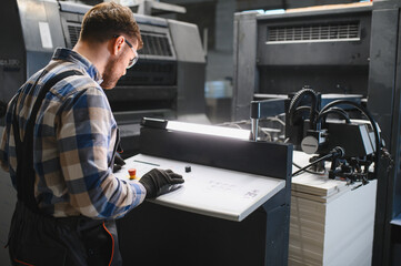 Obraz premium Worker operating industrial offset printing machine in factory