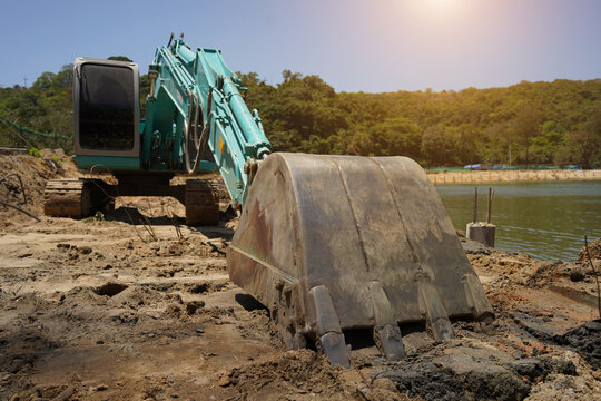Building process city levee. Excavator dredging pond bank