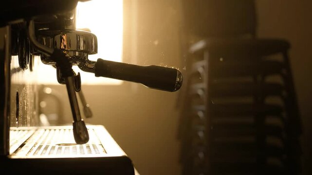 Close up of an espresso machine in a dimly lit abandoned cafe with sunlight streaming through a window illuminating dust particles floating in the air of an empty shop
