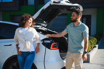 Fototapeta premium Couple charging electric car at home, embracing green energy and sustainable lifestyle