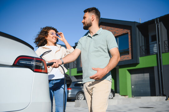 Couple charging electric car at home near modern house