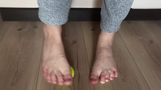 Woman massaging her foot with a spiky plantar fasciitis massage ball for pain relief and myofascial release, performing a therapeutic exercise for flat feet at home