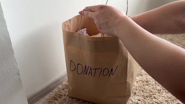 Woman putting used clothes into a paper bag for donation, promoting recycling, sustainable living, and conscious consumption for charity and helping people in need