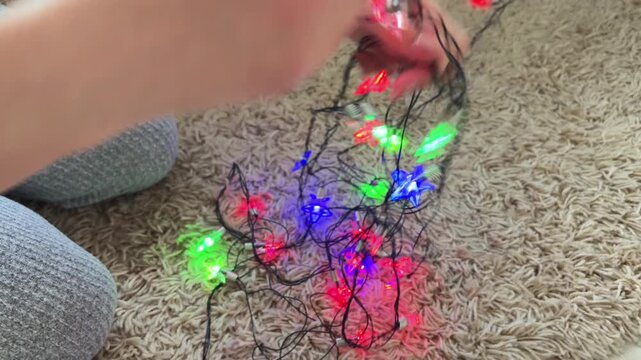 Woman untangling tangled christmas star lights for holiday decoration at home, preparing for new year celebration while sitting on a carpet in a cozy atmosphere