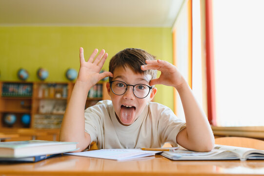 Naughty pupil sticking out tongue while studying in classroom
