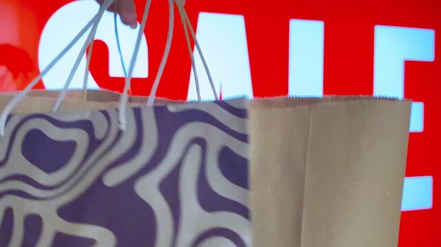 Person holding shopping bags walking past a large red sale sign in a retail store during black friday, symbolizing consumerism, promotion, and big discounts