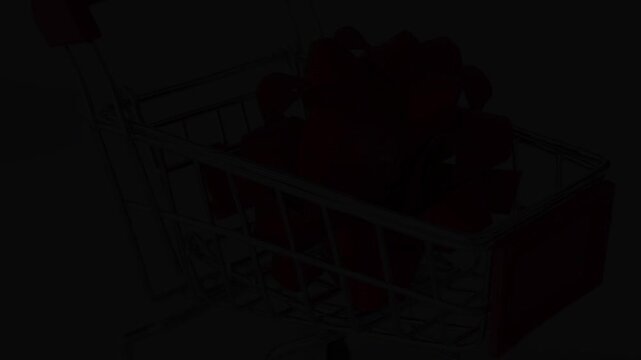 Red gift bow falling into a miniature shopping cart symbolizing holiday shopping, consumerism, and christmas promotions on a clean white background, representing retail sales