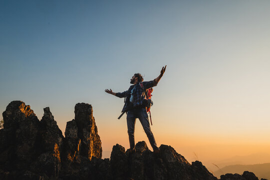 Hiker stands atop jagged peaks, arms raised in triumph