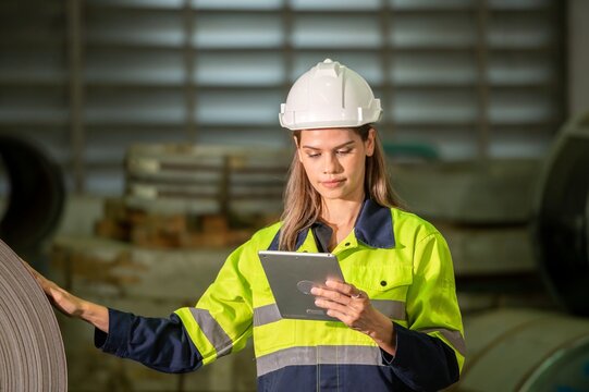 Worker inspecting metal sheet machine performance checklist operation system inspection in factory Female engineer wearing hardhat and safety jacket checking inventory on tablet at storage site