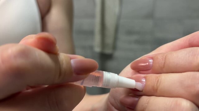 Close up of a woman applying nourishing cuticle oil with a pen applicator to her nude polished nails for hydration, strengthening, and promoting healthy growth