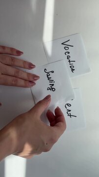 Person prioritizing handwritten notes for rent, saving, and vacation expenses, demonstrating budget planning and financial management for important life goals and choices