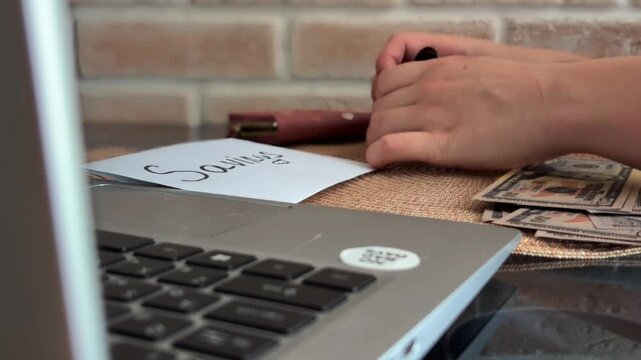 Woman's hands counting dollar bills, calculating budget, and placing cash into savings envelope for financial planning, investment, and future security at home office desk