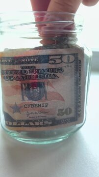 Person placing united states fifty dollar bills into a transparent glass jar, a conceptual representation of accumulating wealth, personal savings, and financial planning