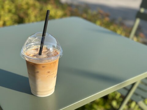 Iced coffee in a takeaway cup on outdoor table in warm sunlight