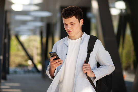 Young man checks his phone while standing under a modern building during daytime