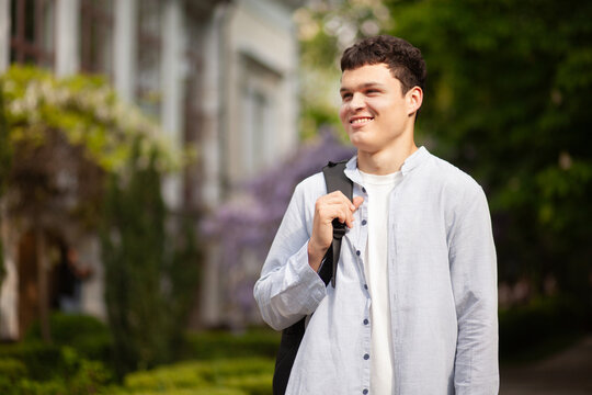 Young man stands in a garden with a bag on his shoulder while smiling in spring