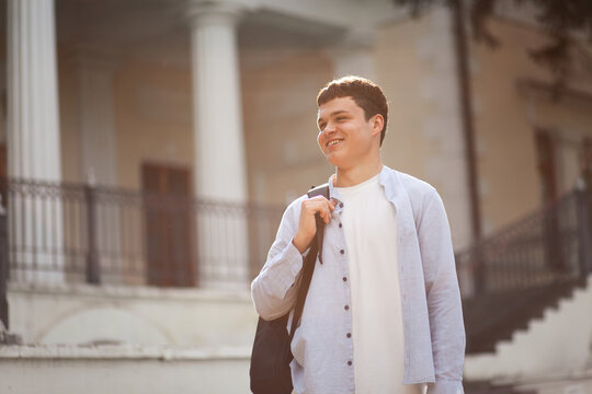 Young man walks outside near a building with white columns during a sunny day in the afternoon