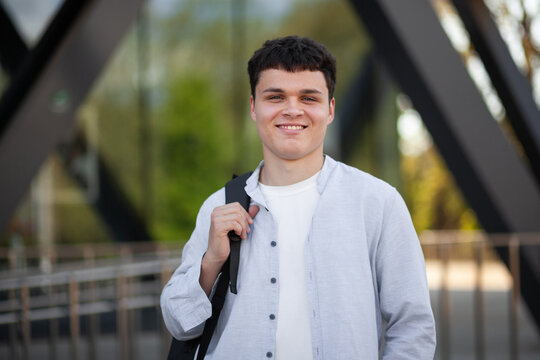 Young man smiles while standing outside a modern building during daylight in a city setting