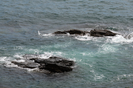 Sea waves crashing over dark rocky reef in clear ocean water