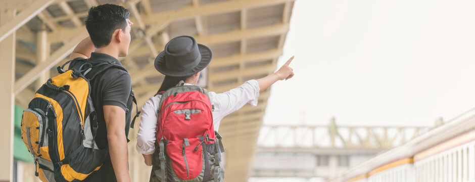 Couple of traveler searching right direction at train station. Asian Backpackers pointing and planning holiday vacation with location map. Travel concept-banner image.