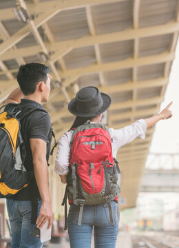 Couple of traveler searching right direction at train station. Asian Backpackers pointing and planning holiday vacation with location map. Travel concept-vertical image.