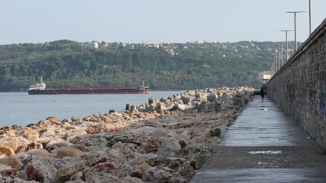 Cargo ship sailing past a breakwater with person walking