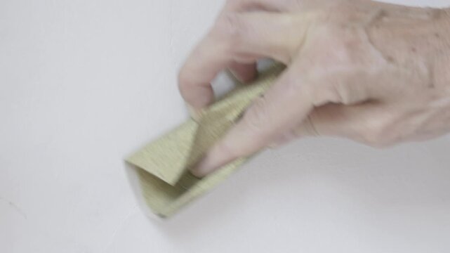 Sanding white wall surface with sandpaper