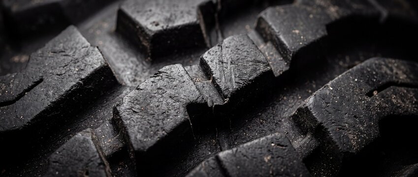 Rugged black all terrain tire tread pattern surface with deep grooves providing high friction and durability for heavy off road vehicles