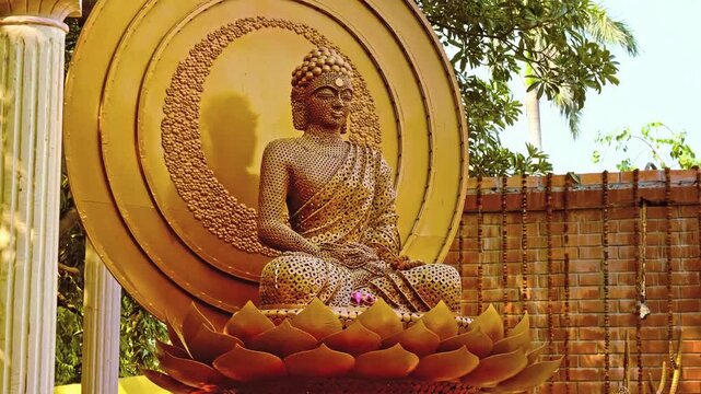 Golden Buddha statue sitting on lotus flower base in peaceful outdoor temple garden setting.