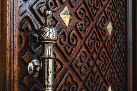 Close up of ornate carved dark wooden door with geometric diamond pattern and brass handle, Islamic architecture concept