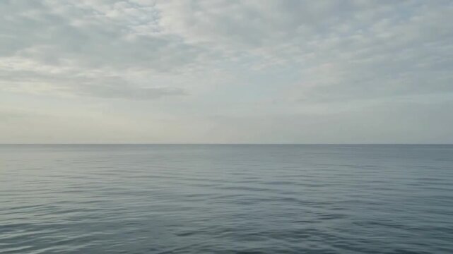 Minimal cinematic footage of a calm ocean meeting a pale overcast sky along a clean horizon.