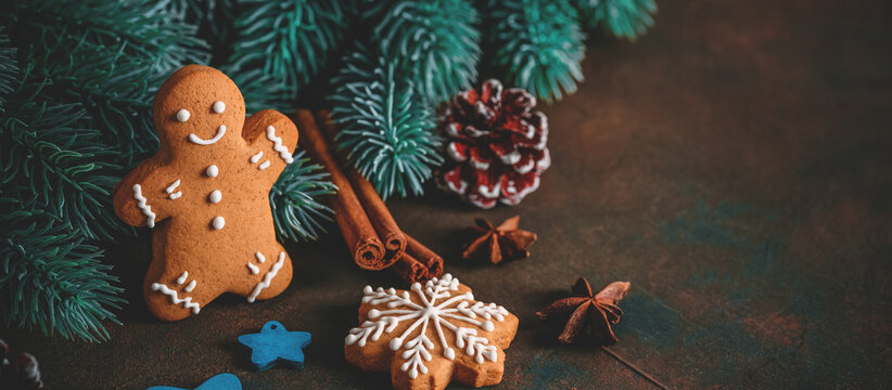 Gingerbread man on dark grunge background with Christmas decorations, fir branches, spices, stars, selective focus, copy space.