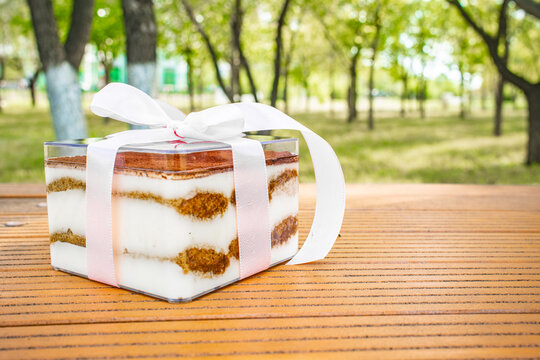 Close up of tiramisu dessert in white tray showing cream and cocoa layers on wooden surface, Italian food concept