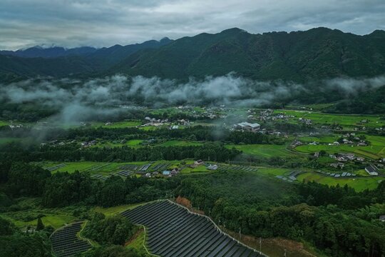 Aerial drone photo of misty mountain valley with solar panels and farmland in Mihama, Mie, Japan