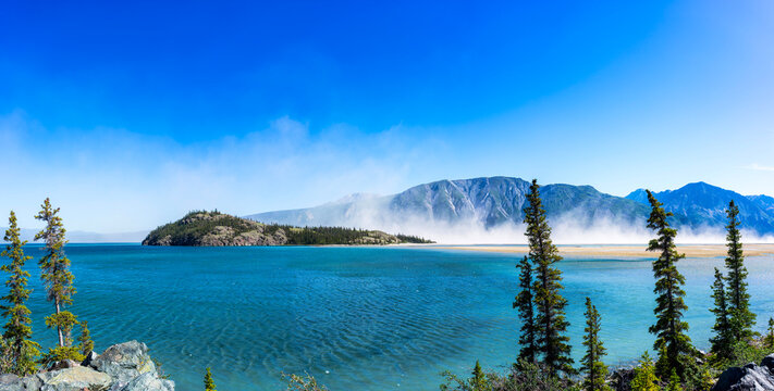 Clouds of dust over Kluane Lake. Dust forms over the former mouth of the Slims River, now dry, as the river has changed direction due to climate change.