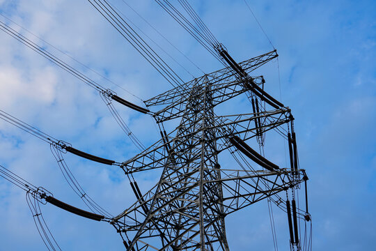 High voltage transmission tower, power pylon against cloudy blue sky