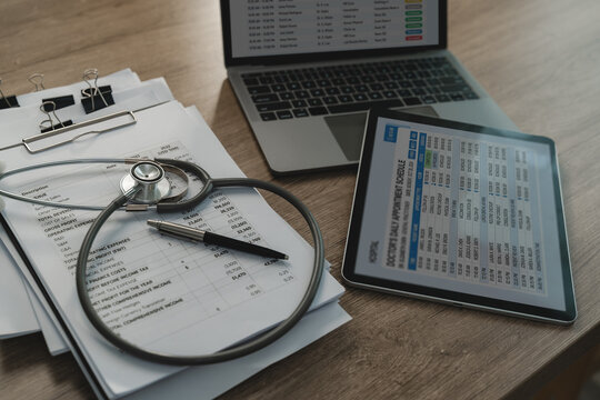 Medical data Stethoscope rests business report beside tablet and laptop screens displaying doctor appointment schedules, healthcare administration and clinical operations planning.
