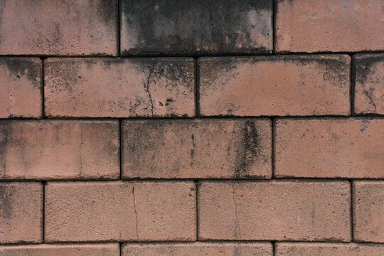 Weathered interlocking brick wall background texture with grunge dark mold stains and cracks.
