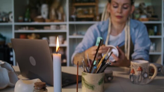 Woman decorates ceramic mug at worktable in pottery studio