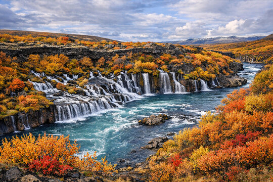 Mountain waterfall and stream flowing through colorful autumn foliage.