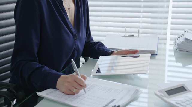 Professional woman using digital tablet for business tasks, typing data and reviewing documents at a modern office desk, symbolizing efficiency and financial management