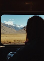 Obraz premium Passenger Silhouette Looking Through Train Window at Snow Capped Mountains and Valley Landscape