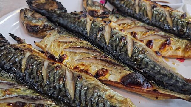 Footage of grilled mackerel cooked in a wood-fired oven being placed on a plate in a restaurant