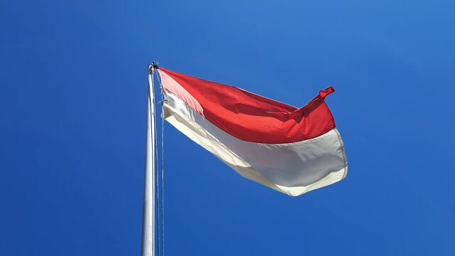 Indonesian red and white flag waving on flagpole against clear blue sky. National symbol, 17 August, independence day, patriotic, proud, wind.