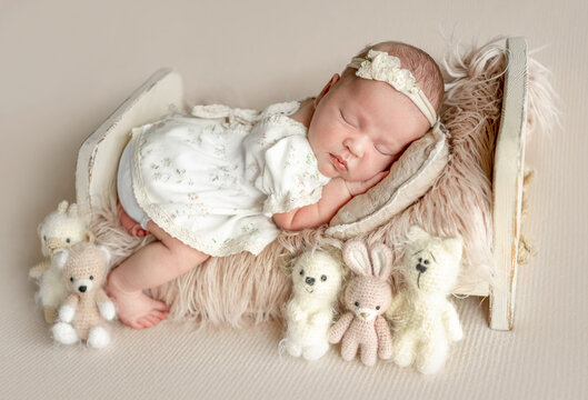 Sleeping infant wearing floral dress rests on soft fur with cute crochet toys in studio
