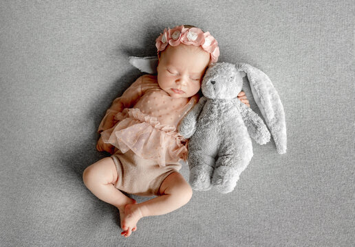 Sleeping newborn rests with a stuffed toy on a gray blanket.