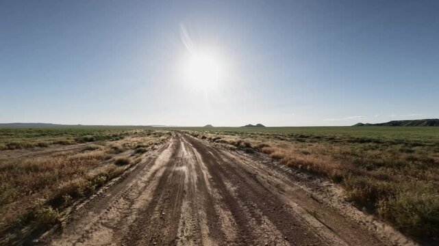 Off-road vehicle traverses dirt path under bright sun in open landscape